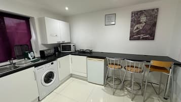 A compact kitchen with a washing machine, microwave, and a small dining area with two stools.