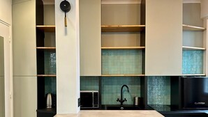 A modern kitchen with a central island, black cabinets, and a black countertop. There are two wicker chairs and a black sink with a faucet. - Charming duplex apartment near Champs-Elysées (Paris)