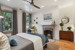 A bedroom with a bed, a fireplace, a ceiling fan, and a view of greenery outside. - Rare 4BR Savannah Retreat | Shared Pool & DT Steps (Savannah)