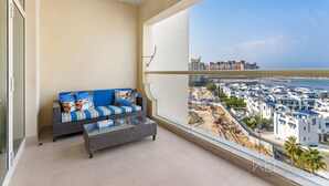 A balcony with a sofa and a coffee table, overlooking a coastal area with buildings and construction.