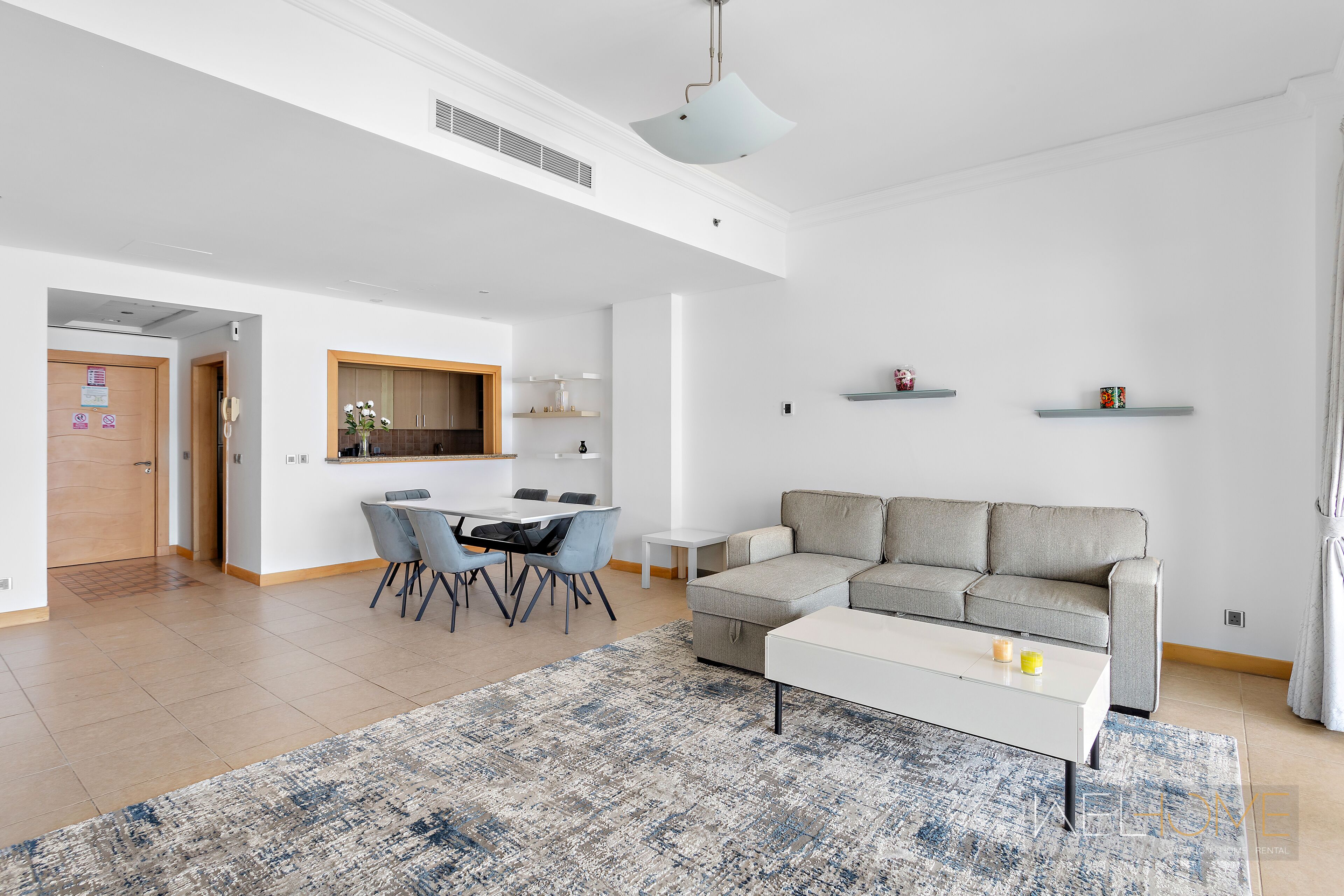 A modern living room with a grey sofa, a white coffee table, and a dining area with chairs and a table.