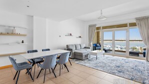 A modern living room with a dining area, large windows, and a view of the sea.