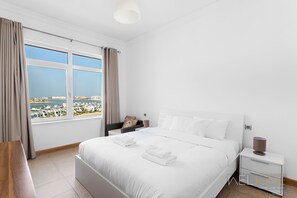 Habitació d'hotel moderna amb un llit gran, una taula de nit i vistes a la ciutat costanera.