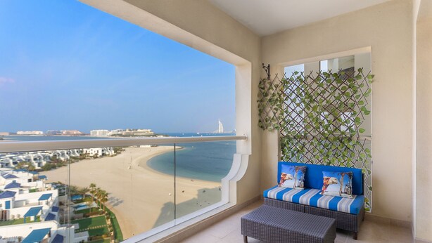 A balcony with a view of the beach and cityscape, a sofa with cushions, and a small table.