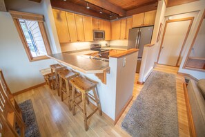A modern kitchen with wooden cabinets, a large island with bar stools, a microwave, and a refrigerator. - Stylish, Mtn Views, 2 parking spots (Keystone)