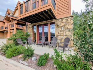 A lodge with a stone facade, wooden balconies, and outdoor seating with Adirondack chairs.