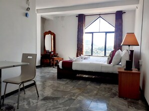 A hotel room with a bed, a desk, a chair, a mirror, a lamp, and a window with curtains. - New Unique View Hotel (Nuwara Eliya)