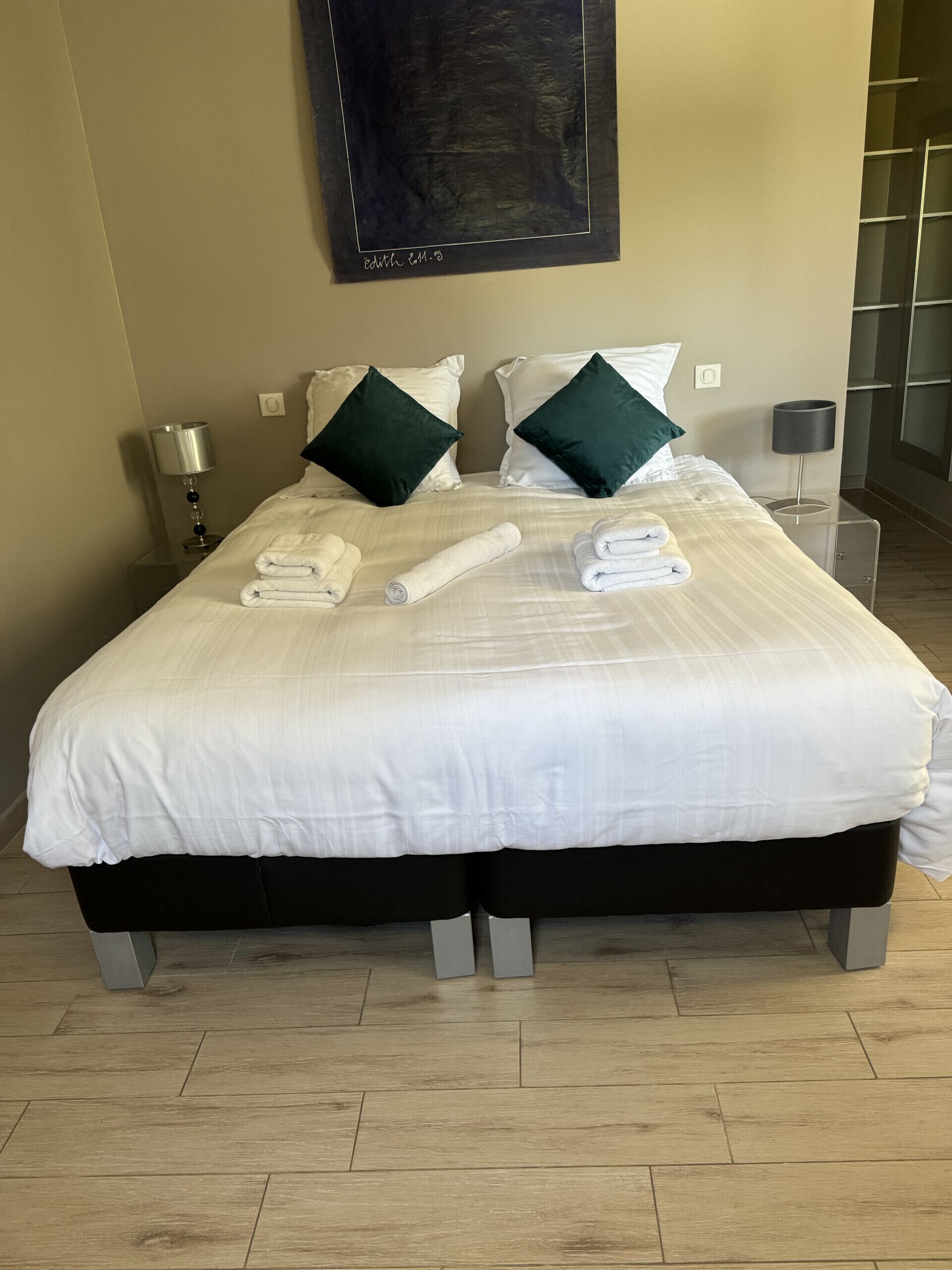 Une chambre d’hôtel avec un grand lit, deux tables de chevet, une œuvre d’art accrochée au mur et un plancher en bois.