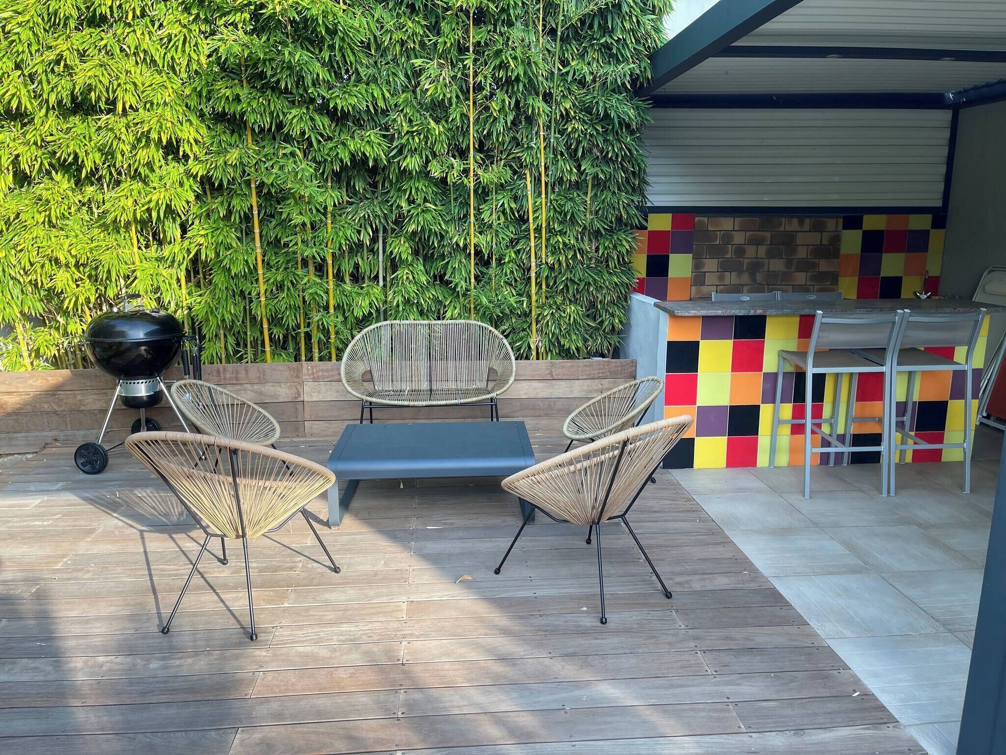 An outdoor patio with a grill, wicker chairs, a table, and a colorful tiled bar area.