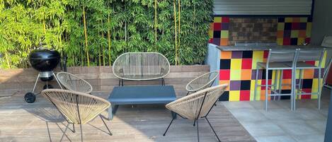 An outdoor patio with a grill, wicker chairs, a table, and a colorful tiled bar area.
