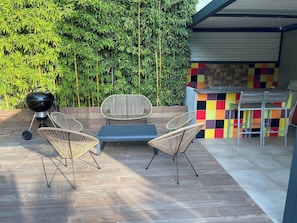 An outdoor patio with a grill, wicker chairs, a table, and a colorful tiled bar area. - Sète, Jolie villa avec piscine à 5 mn des plages (Sète)