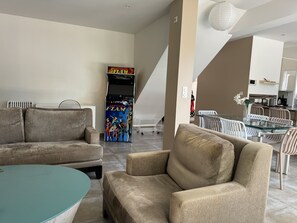 A living room with a sofa, armchair, and a glass-top coffee table. There is a retro video game machine in the background. - Sète, Jolie villa avec piscine à 5 mn des plages (Sète)