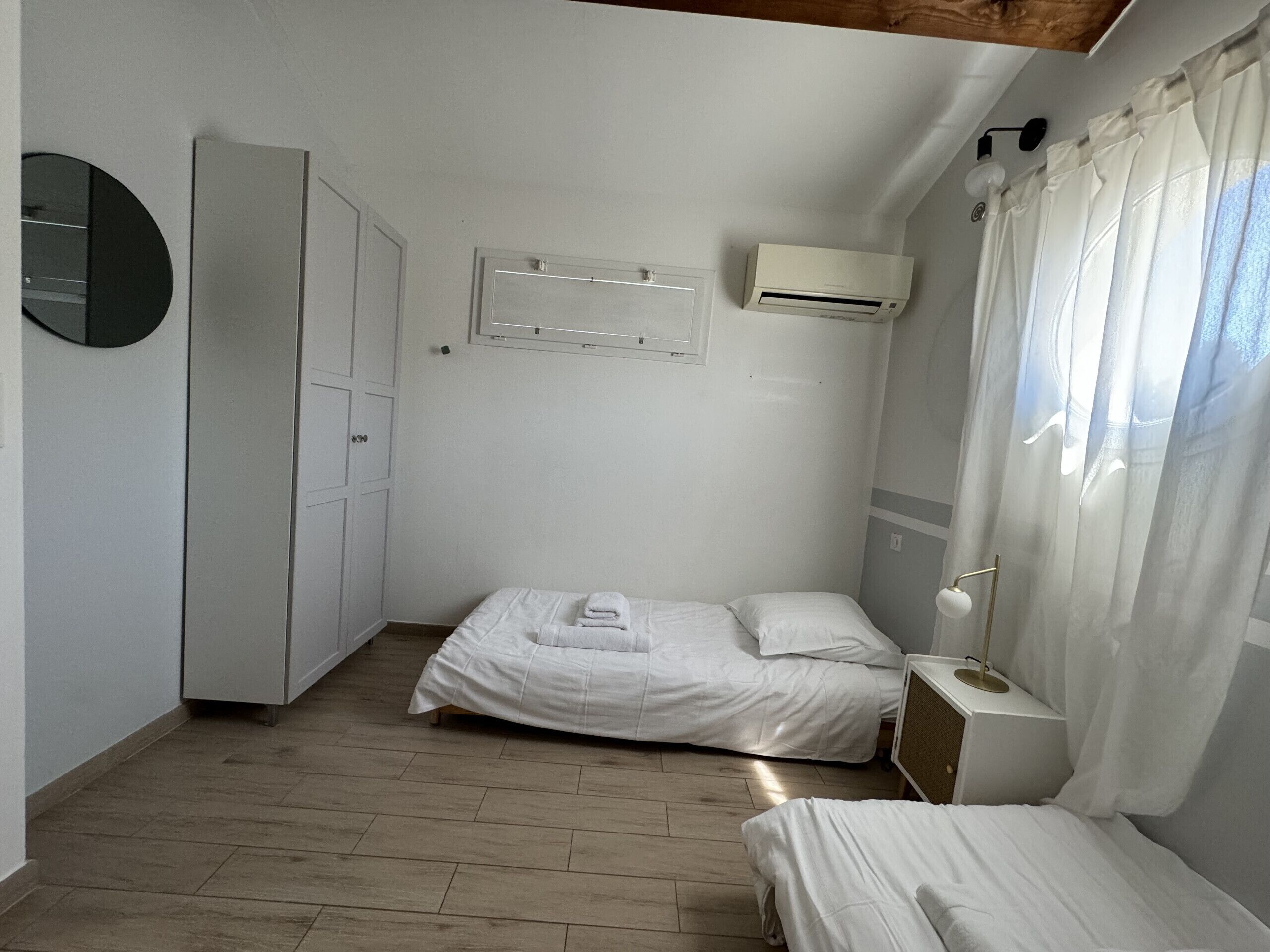 A room with a bed, a wardrobe, an air conditioning unit, and a bedside table with a lamp.
