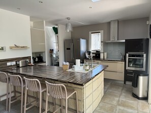 A modern kitchen with a central island, bar stools, stainless steel appliances, and a window providing natural light.