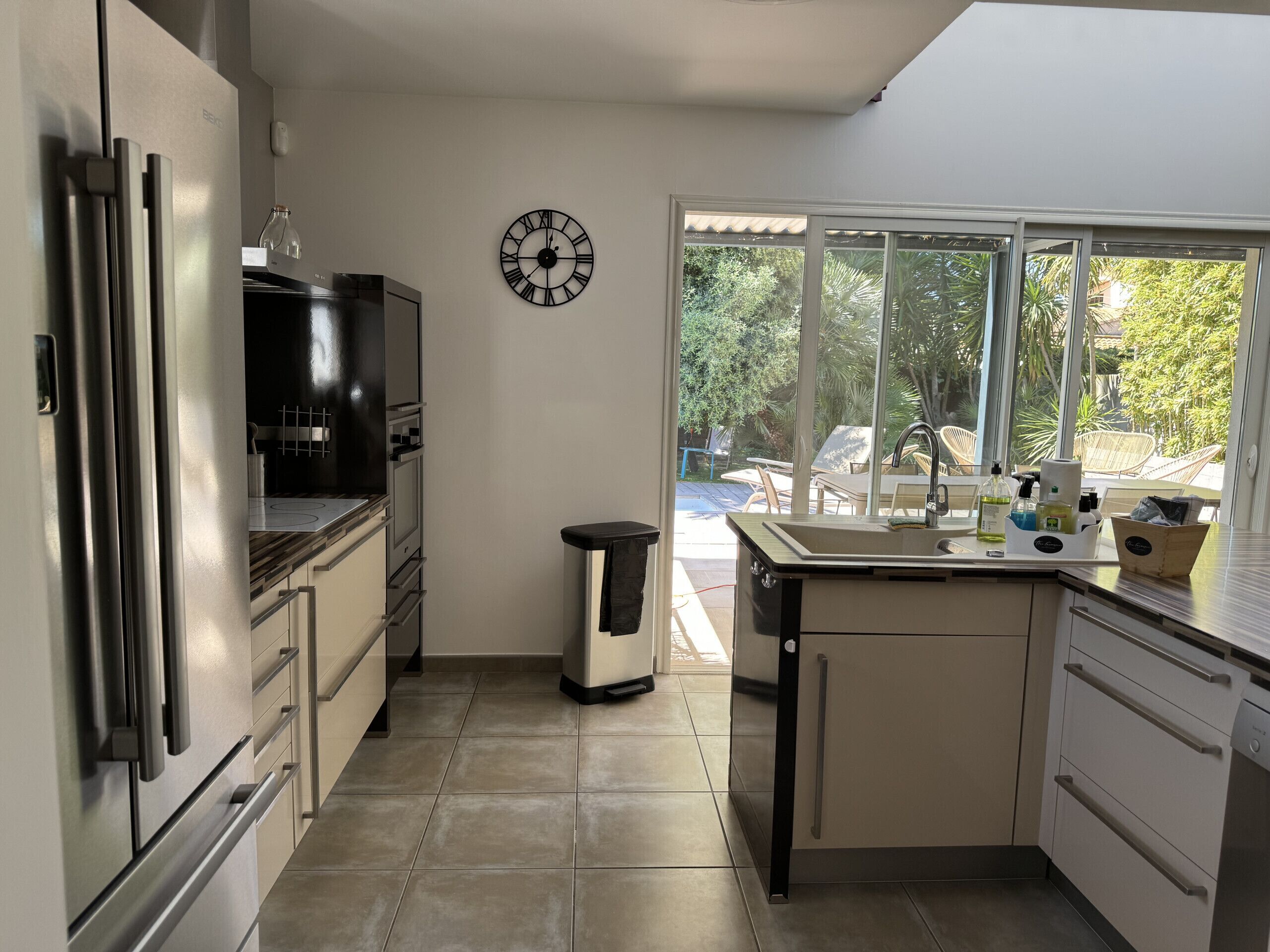 A modern kitchen with a built-in oven, a sink, and a clock on the wall.