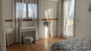 A bedroom with a bed, a desk, a chair, and an air conditioning unit.