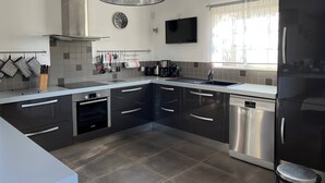 A modern kitchen with black cabinets, stainless steel appliances, a black and white pendant light, a clock, and a window with sheer curtains.