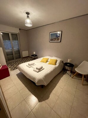 Hotelkamer met een bed, een stoel, een klein tafeltje, een foto aan de muur en uitzicht door de deur.