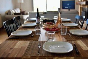 Taula de menjador preparada amb plats, gots, coberts i una ampolla de vi, amb un bol de cireres i una barra de pa sobre la taula.
