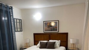 Una camera d'hotel con un letto grande, due comodini, un tavolino e un quadro appeso alla parete, con una tenda sul lato sinistro.