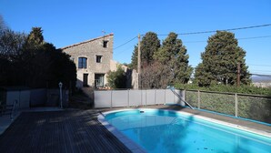 Una piscina con bordo in legno, un edificio in pietra e alberi alti sullo sfondo.