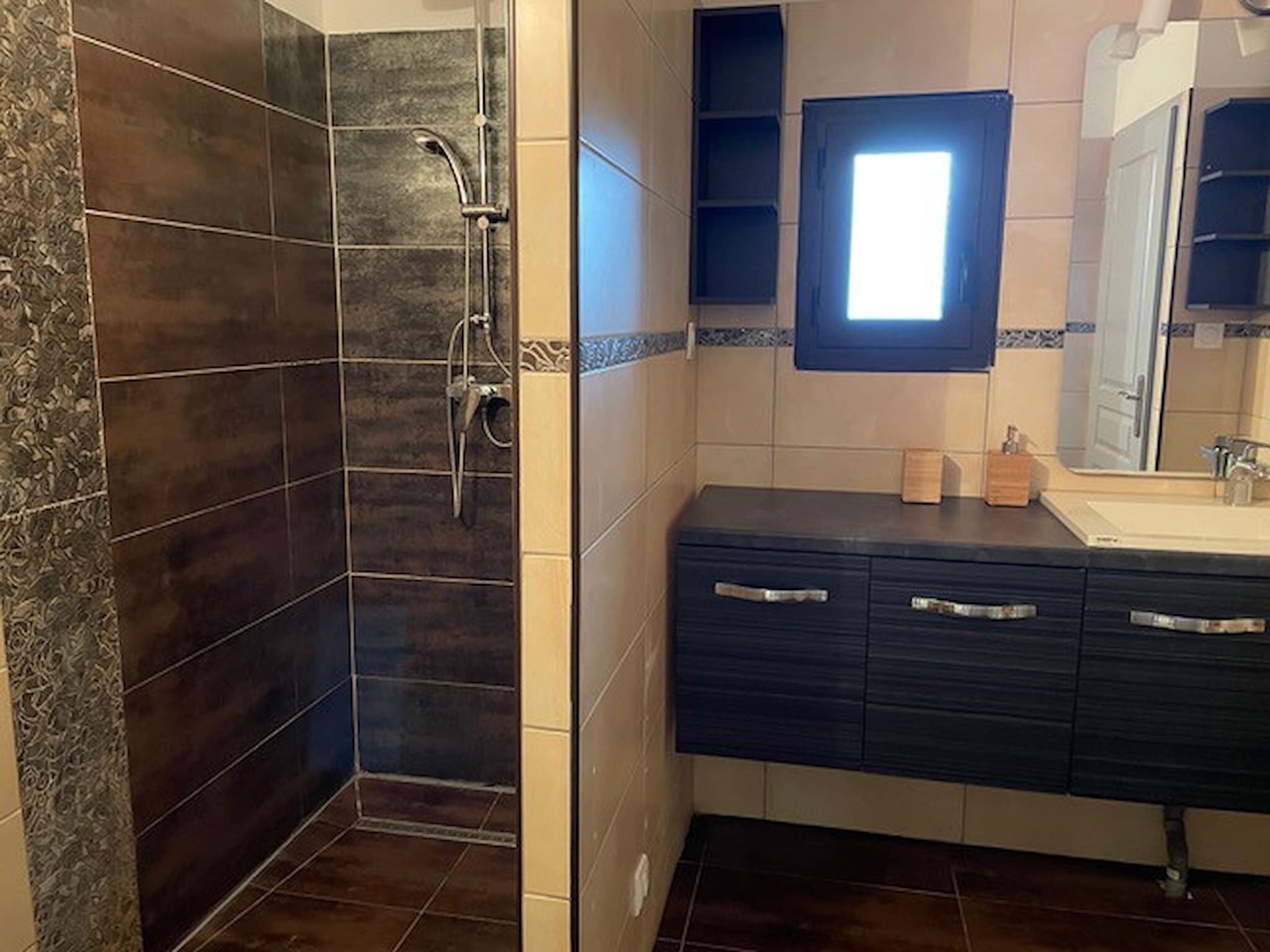 Une salle de bain avec une douche, des carreaux de couleur sombre, un lavabo et un miroir.