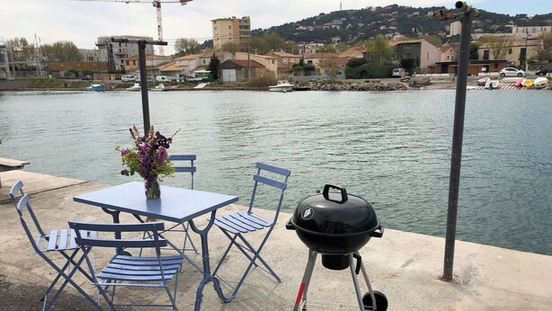 Een tafel met stoelen en een barbecue aan het water.