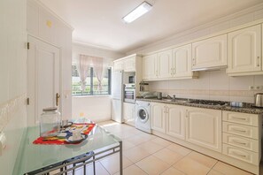 Una cocina compacta con armarios blancos, horno empotrado, lavadora y una mesa de vidrio con un mantel individual colorido.