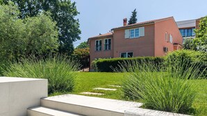 A modern two-story house with a red facade, a well-maintained lawn, and a concrete staircase leading to the entrance.