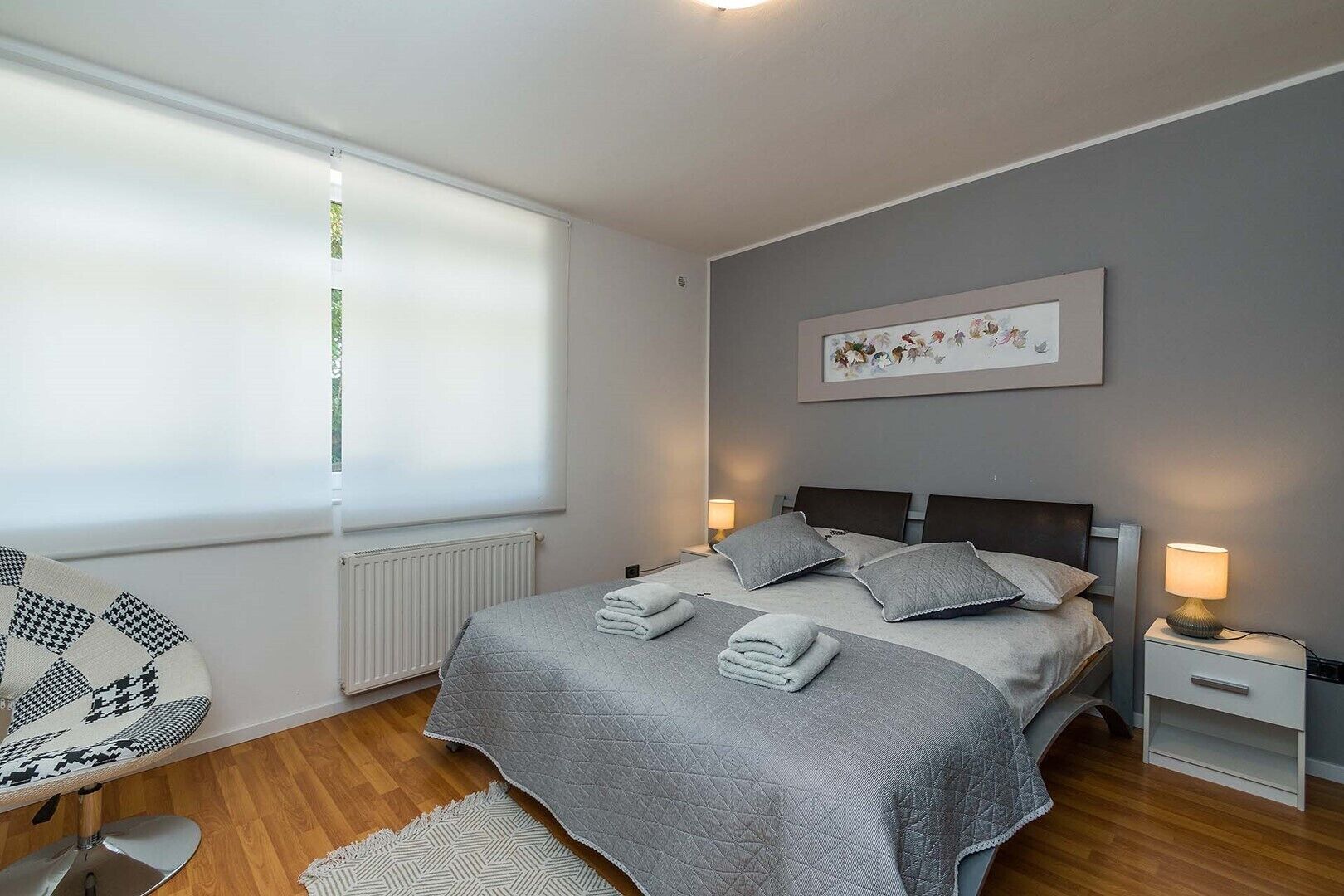 A modern bedroom with a large bed, bedside lamps, a radiator, and a window with blinds.