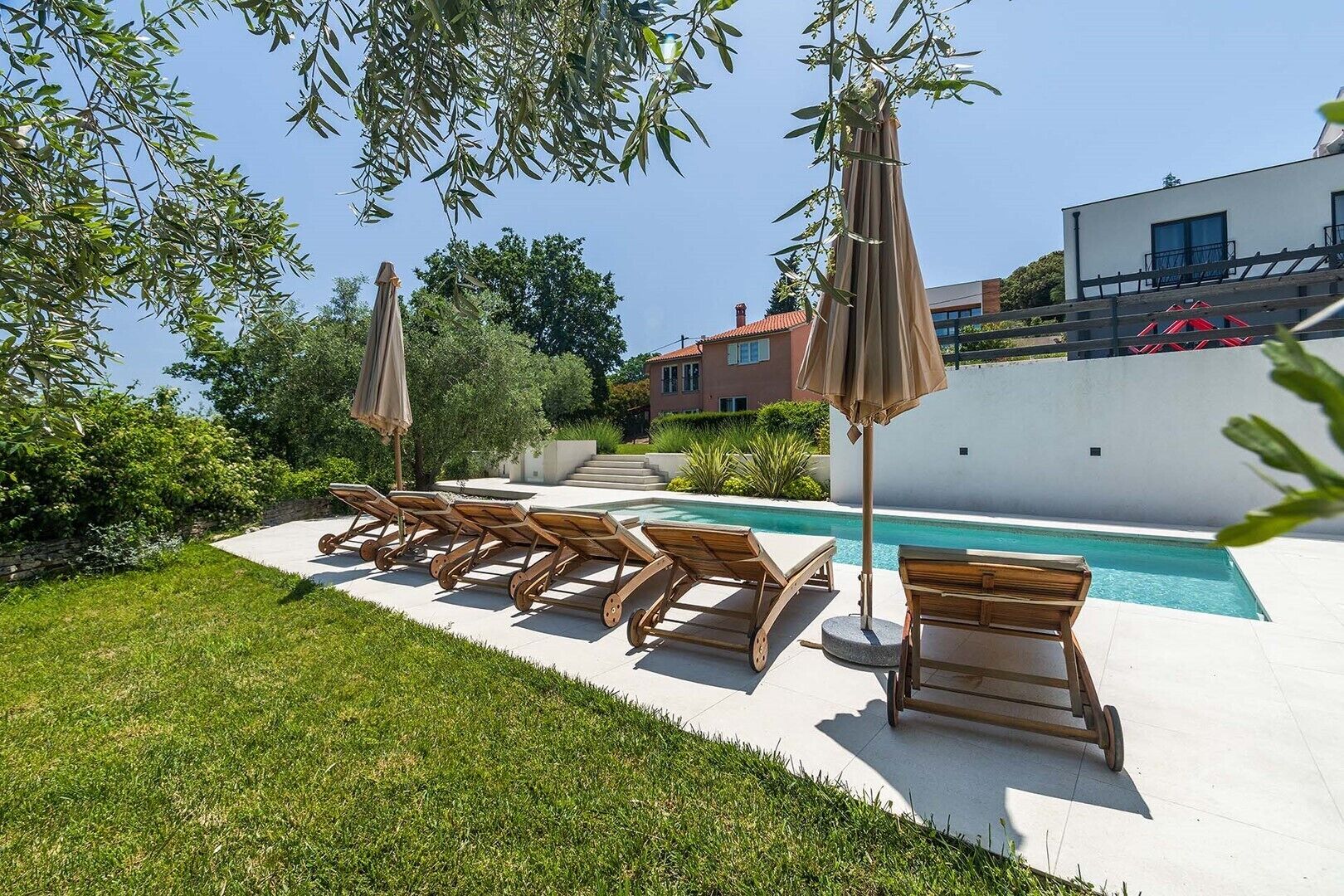 Un espace aménagé au bord de la piscine, avec des chaises longues et des parasols, une piscine à l’eau d’un bleu limpide et un bâtiment moderne en arrière-plan.