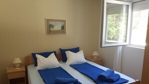 A double bed with blue and white bedding, two nightstands with lamps, a framed picture on the wall, and a window with a view of greenery. - BlueSun
Two Bedroom Apartment with terrace  (Zaton)