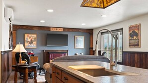 A kitchen with a built-in island, a fireplace, and a large window. - Newly Built Rustic Cabin w/ Mountain & Pond Views (Kalispell)