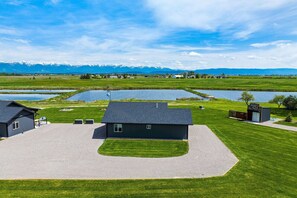 A modern building with a flat roof, surrounded by a well-maintained lawn and a small pond. - Newly Built Rustic Cabin w/ Mountain & Pond Views (Kalispell)