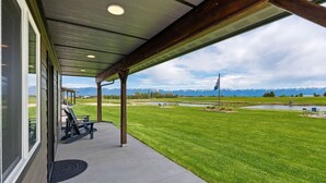 A covered patio with a view of a grassy area and mountains. - Newly Built Rustic Cabin w/ Mountain & Pond Views (Kalispell)
