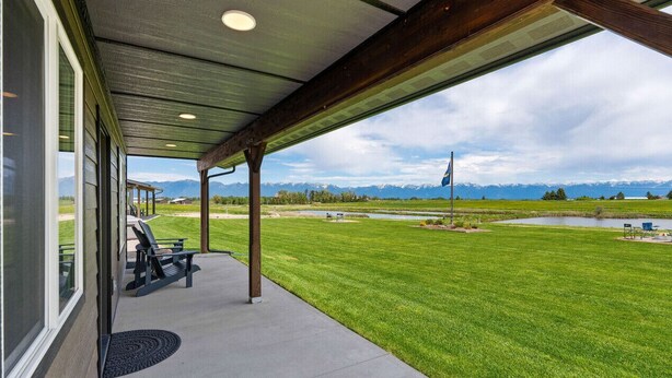 A covered patio with a view of a grassy area and mountains. - Newly Built Rustic Cabin w/ Mountain & Pond Views (Kalispell)
