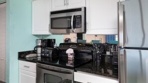Una cocina moderna con armarios blancos, un microondas de acero inoxidable, un refrigerador, una estufa y una cafetera.