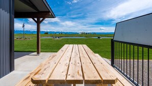 A wooden picnic table on a balcony with a view of a lake and mountains in the distance. - Charming Cabin w/ Wildlife & Mountain Views (Kalispell)