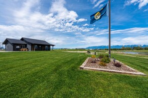 A house with a flagpole, a lawn, and mountains in the background.