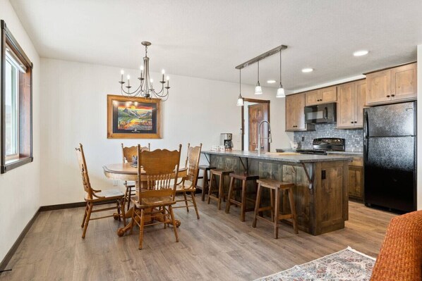 A kitchen with wooden cabinets, a central island, bar stools, and a chandelier.
