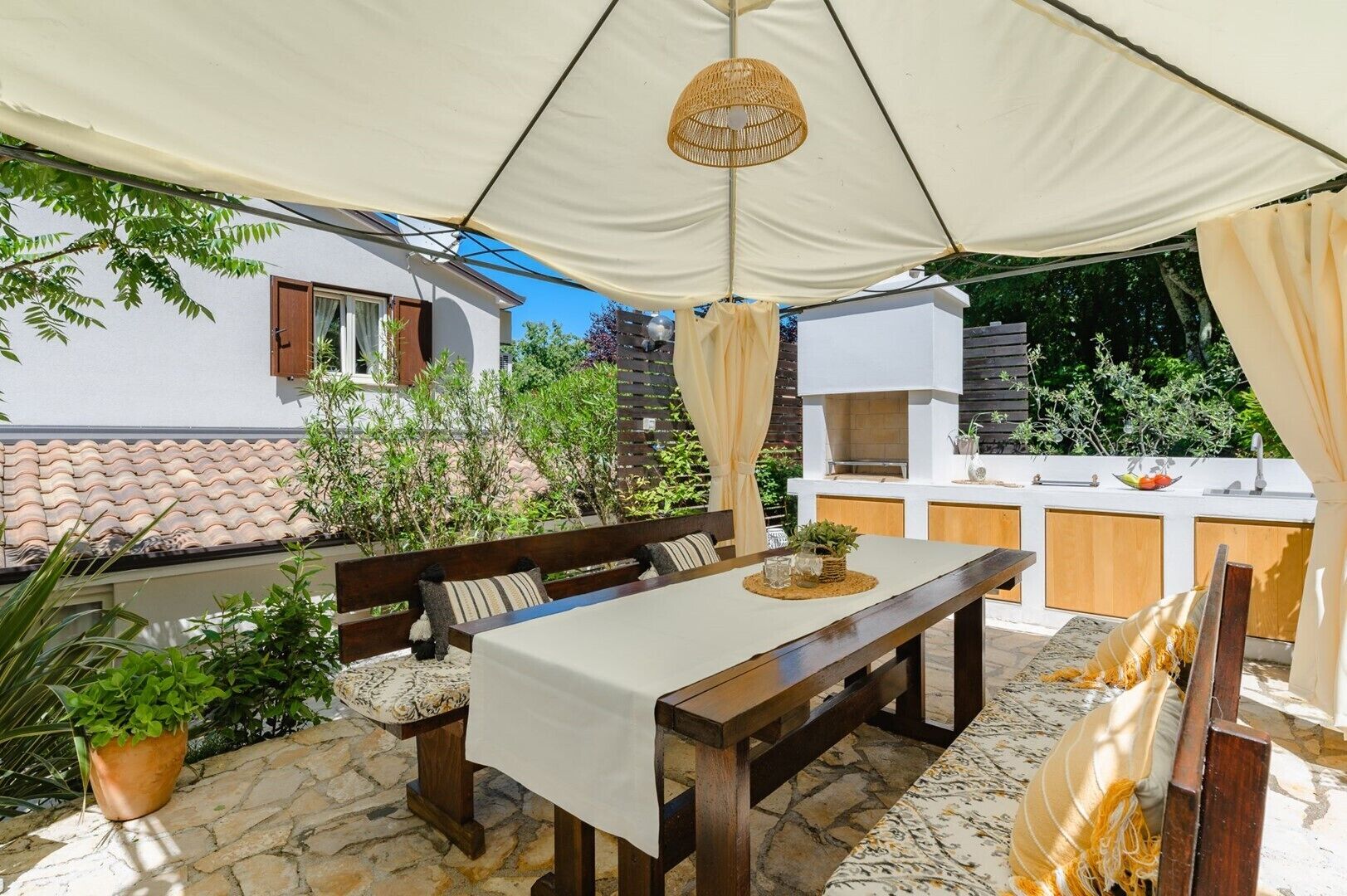 An outdoor patio with a dining table, benches, and a built-in kitchen area.