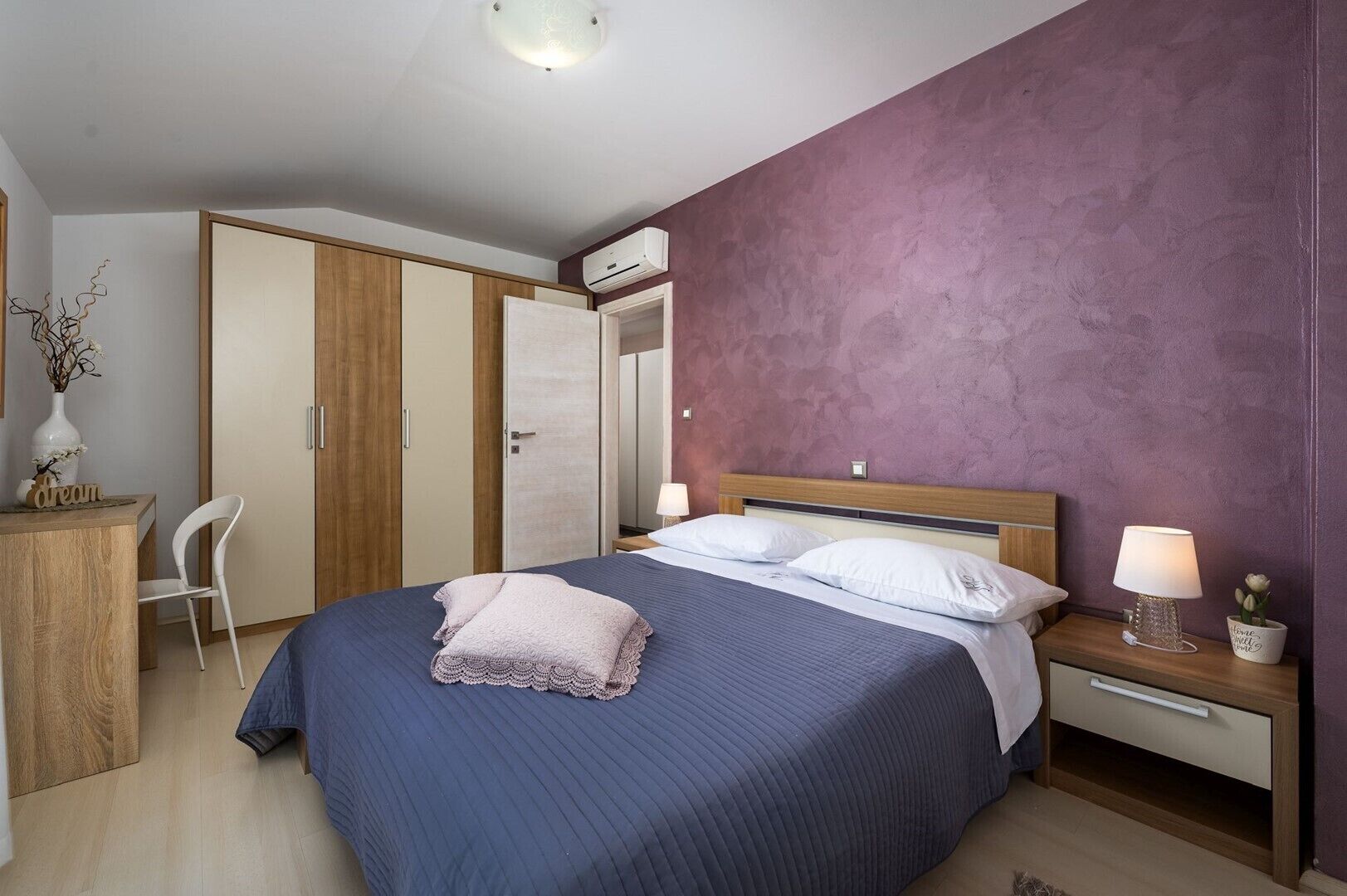 A bedroom with a bed, bedside table, nightstand, wardrobe, and a desk with a chair.