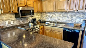 Una cocina con encimeras de granito, armarios de madera, electrodomésticos de acero inoxidable y salpicadero de azulejos.