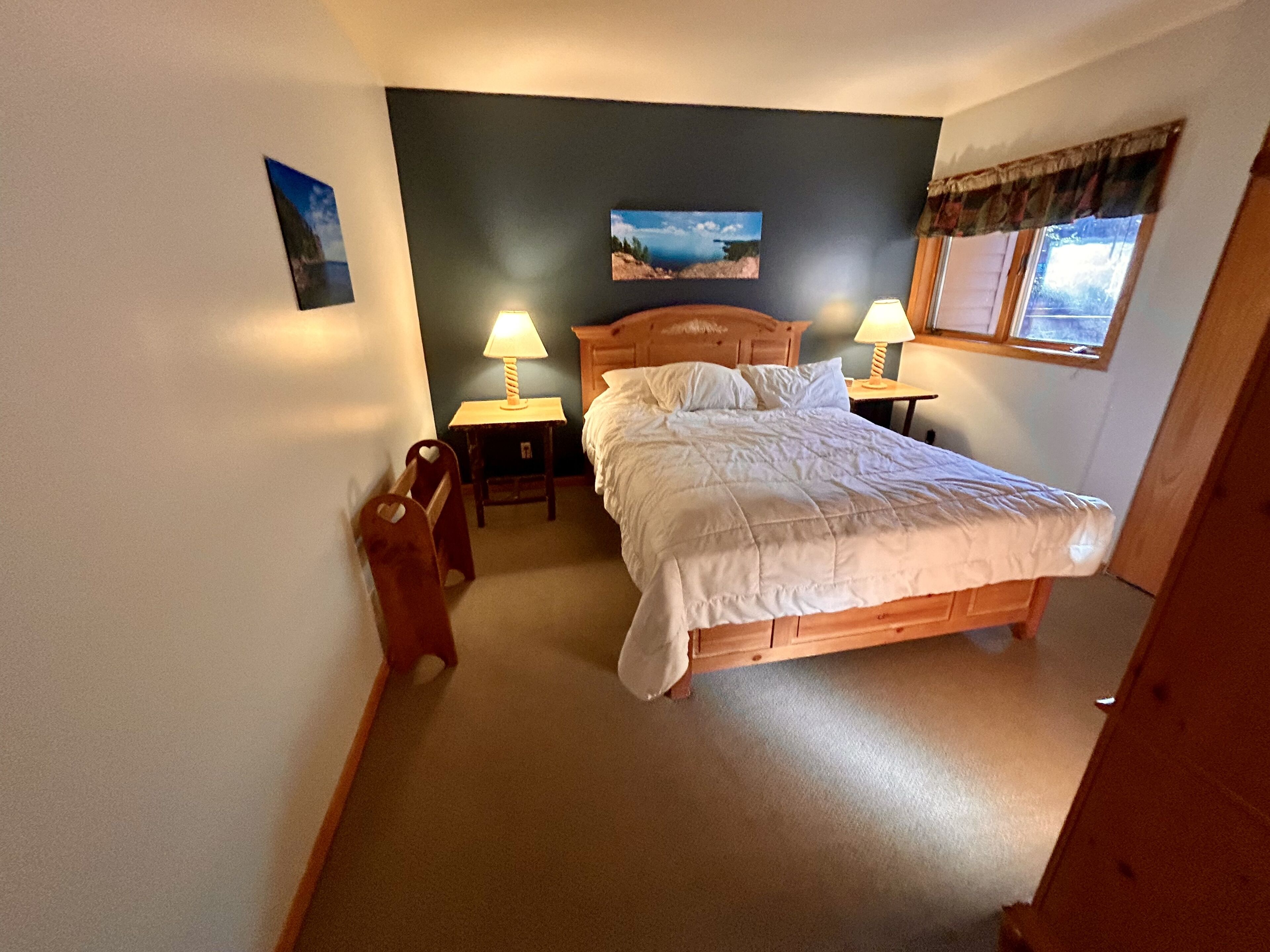 Une chambre à coucher avec un lit en bois, deux lampes de chevet, une table de chevet, une petite chaise et une fenêtre avec des rideaux.