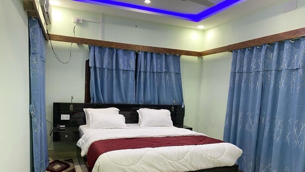 A bedroom with a bed, curtains, a bedside table, and a nightstand. - Royalwood City Inn (Biratnagar)
