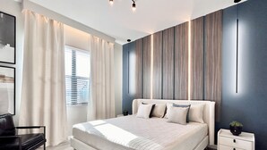 A modern bedroom with a large bed, a bedside table, a chair, and a window with curtains. - Paradiso Grande 8BR Luxury Home, Cinema, PS5 Loft, Pvt Pool, BBQ, Near Parks! (Orlando)
