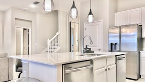 A modern kitchen with a central island, stainless steel appliances, and pendant lighting. - Paradiso Grande 8BR Luxury Home, Cinema, PS5 Loft, Pvt Pool, BBQ, Near Parks! (Orlando)