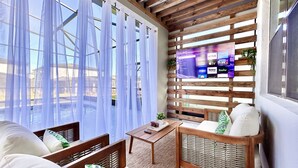 A cozy room with a wooden ceiling, a large window with sheer curtains, a TV mounted on the wall, and a comfortable seating area with a sofa and chairs. - Paradiso Grande 8BR Luxury Home, Cinema, PS5 Loft, Pvt Pool, BBQ, Near Parks! (Orlando)