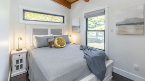 A bedroom with a bed, nightstands, a window with a view, and artwork on the wall.