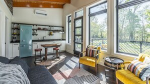 A modern kitchen with a blue refrigerator, a dining area with a yellow chair, and large windows offering a view of the outdoors.
